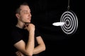 Man and dart board with a quill pen stuck in the center of the target on a black background in a low key Royalty Free Stock Photo