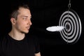 Man and dart board with a quill pen stuck in the center of the target on a black background in a low key Royalty Free Stock Photo