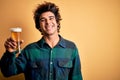 Young handsome man drinking glass of beer standing over isolated yellow background with a happy face standing and smiling with a Royalty Free Stock Photo