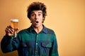 Young handsome man drinking glass of beer standing over isolated yellow background scared in shock with a surprise face, afraid Royalty Free Stock Photo