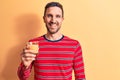 Young handsome man drinking glass of healthy orange juice over isolated yellow background looking positive and happy standing and Royalty Free Stock Photo