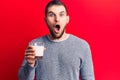 Young handsome man drinking glass of milk scared and amazed with open mouth for surprise, disbelief face Royalty Free Stock Photo