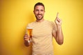 Young handsome man drinking a pint glass of beer over isolated yellow background very happy pointing with hand and finger to the Royalty Free Stock Photo