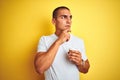 Young handsome man drinking a take away glass of coffee over yellow isolated background serious face thinking about question, very