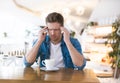 Young handsome man drinks coffee during his lunch break in the cafe looks tired after haed working day, tough life concept