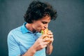 Young handsome man eating a healthy burger. Hungry man in a fast food restaurant eating a hamburger outdoors. Man with curly hair