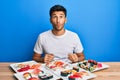 Young handsome man eating sushi sitting on the table making fish face with lips, crazy and comical gesture Royalty Free Stock Photo