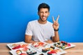 Young handsome man eating sushi sitting on the table smiling with happy face winking at the camera doing victory sign Royalty Free Stock Photo