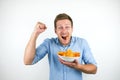 Young handsome man eats paprika chips holding his fist up on isolated white background Royalty Free Stock Photo