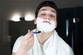 Young handsome man with foam on his face shaving with razor in bathroom in the morning everyday routine Royalty Free Stock Photo