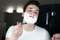 Young handsome man with foam on his face shaving with razor in bathroom in the morning looking bold everyday routine Royalty Free Stock Photo