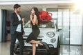 Young handsome man gives keys from brand new car he presented to his beautiful grateful wife standing in dealership