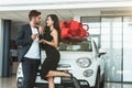 Young handsome man gives keys from brand new car he presented to his beautiful woman standing in dealership center Royalty Free Stock Photo