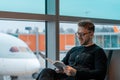 Young handsome man with glasses reading a book while waiting for boarding at air jet in airport. Royalty Free Stock Photo