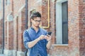 A young handsome man with glasses walks down a city street holding a mobile phone, looking for a place and a street on a GPS Royalty Free Stock Photo