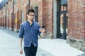 A young handsome man with glasses walks down a city street holding a mobile phone, looking for a place and a street on a GPS Royalty Free Stock Photo