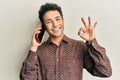 Young handsome man having conversation talking on the smartphone doing ok sign with fingers, smiling friendly gesturing excellent Royalty Free Stock Photo