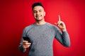 Young handsome man having conversation using smartphone over red background surprised with an idea or question pointing finger Royalty Free Stock Photo