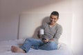 young handsome man having a cup of coffee on bed and using mobile phone. He is smiling. Home, indoors Royalty Free Stock Photo