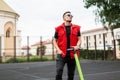 Young handsome man hipster in a stylish red jeans vest in black jeans in sunglasses stands with an electric scooter Royalty Free Stock Photo
