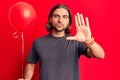 Young handsome man holding balloon with open hand doing stop sign with serious and confident expression, defense gesture