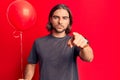 Young handsome man holding balloon pointing with finger to the camera and to you, confident gesture looking serious Royalty Free Stock Photo