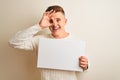 Young handsome man holding banner standing over isolated white background with happy face smiling doing ok sign with hand on eye Royalty Free Stock Photo