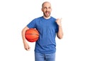 Young handsome man holding basketball ball pointing thumb up to the side smiling happy with open mouth Royalty Free Stock Photo