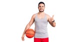 Young handsome man holding basketball ball smiling happy and positive, thumb up doing excellent and approval sign Royalty Free Stock Photo