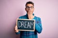 Young handsome man holding blackboard with dream message over pink background cover mouth with hand shocked with shame for Royalty Free Stock Photo