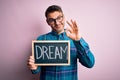 Young handsome man holding blackboard with dream message over pink background doing ok sign with fingers, excellent symbol Royalty Free Stock Photo