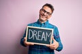 Young handsome man holding blackboard with dream message over pink background with a happy face standing and smiling with a Royalty Free Stock Photo