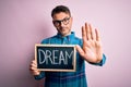 Young handsome man holding blackboard with dream message over pink background with open hand doing stop sign with serious and Royalty Free Stock Photo