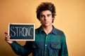 Young handsome man holding blackboard with strong word over isolated yellow background with a confident expression on smart face Royalty Free Stock Photo