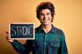 Young handsome man holding blackboard with strong word over isolated yellow background with a happy face standing and smiling with Royalty Free Stock Photo