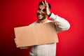 Young handsome man holding blank cardboard banner over isolated red background with happy face smiling doing ok sign with hand on Royalty Free Stock Photo