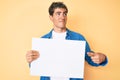 Young handsome man holding blank empty banner smiling looking to the side and staring away thinking