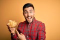 Young handsome man holding bowl with potato chips over isolated yellow background with angry face, negative sign showing dislike Royalty Free Stock Photo