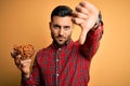 Young handsome man holding bowl with potato chips over isolated yellow background with a happy face standing and smiling with a Royalty Free Stock Photo