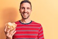 Young handsome man holding bowl of potato chips standing over isolated yellow background looking positive and happy standing and Royalty Free Stock Photo