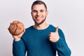 Young handsome man holding bread smiling happy and positive, thumb up doing excellent and approval sign Royalty Free Stock Photo