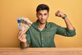 Young handsome man holding canadian dollars strong person showing arm muscle, confident and proud of power