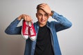 Young handsome man holding casual sneakers standing over isolated white background stressed with hand on head, shocked with shame Royalty Free Stock Photo