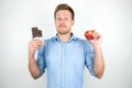 Young handsome man holding chocolate bar in one hand and fresh apple in another on  white background Royalty Free Stock Photo