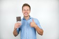 Young handsome man holding chocolate bar showing like sign smiling on  white background Royalty Free Stock Photo
