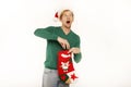Young handsome man holding christmas sock in red santa hat on white studio background