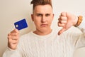 Young handsome man holding credit card over isolated white background with angry face, negative sign showing dislike with thumbs Royalty Free Stock Photo