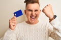 Young handsome man holding credit card over isolated white background annoyed and frustrated shouting with anger, crazy and Royalty Free Stock Photo