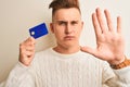 Young handsome man holding credit card over isolated white background with open hand doing stop sign with serious and confident Royalty Free Stock Photo