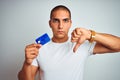 Young handsome man holding credit card over white isolated background with angry face, negative sign showing dislike with thumbs Royalty Free Stock Photo